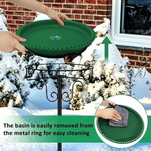 Person removing green bird bath basin from metal stand in snowy garden.