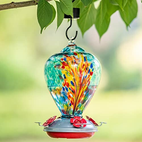 Glass hummingbird feeder with vibrant colors hanging from a tree.