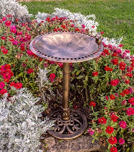 Bronze bird bath surrounded by vibrant flowers in a garden.