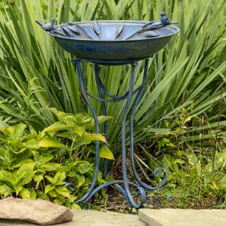 Blue decorative bird bath on a stand in a garden setting.