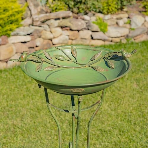 Green bird bath with leaf and bird design in a garden