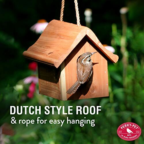 A wooden birdhouse with a Dutch style roof and a bird perched at the entrance.